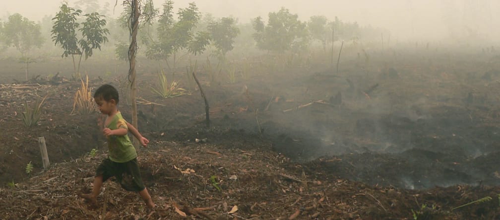 Een kindje loopt over smeulende veenbodem in Katingan, Borneo